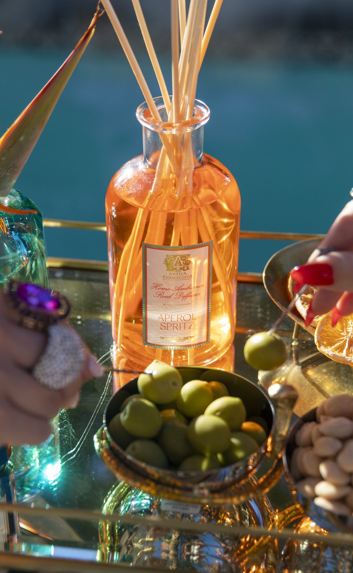 The Aperol Spritz diffuser over a bowl of castelvetrano olives, hands reaching in.
