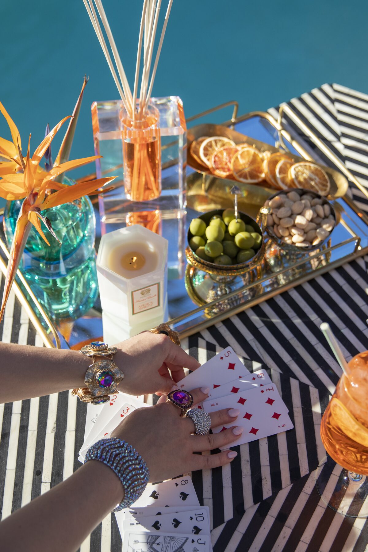 A card game beside the crystal diffuser and a lit candle, amethyst rings and pearl bracelets in play.
