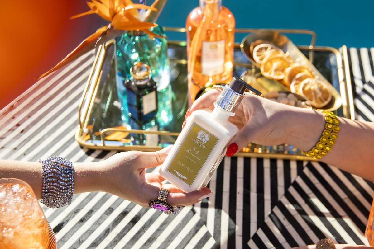 The Grapefruit body moisturiser passed hand to hand over the striped table, the mirrored tray behind.