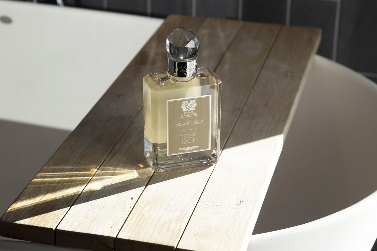 The Desert Sage bubble bath bottle on a teak board laid across a white tub.