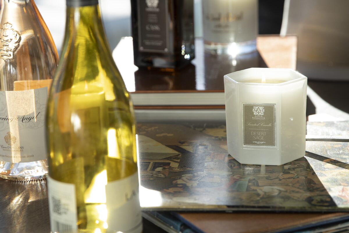 The Desert Sage candle among wine bottles and art books on a sunlit table.