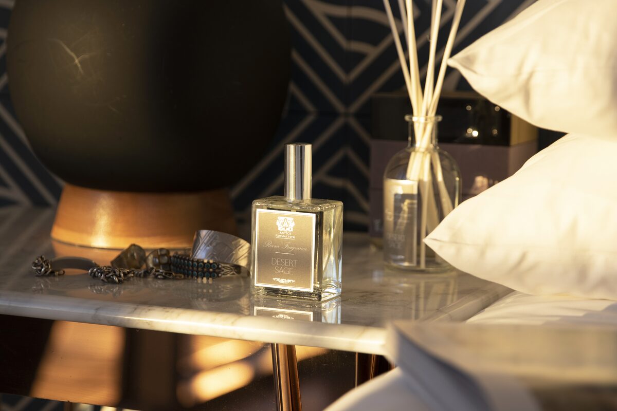 The Desert Sage fine fragrance bottle on a bedside table in warm lamplight, jewellery scattered beside it.