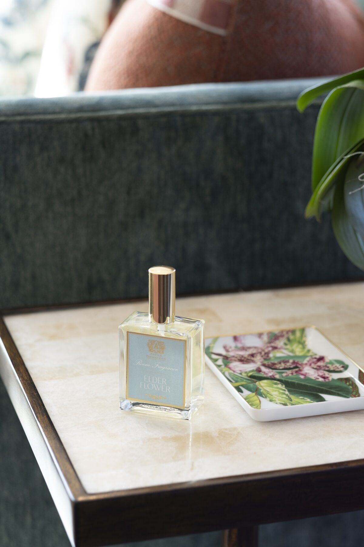The room fragrance on a marble side table against green velvet, a botanical dish beside it.