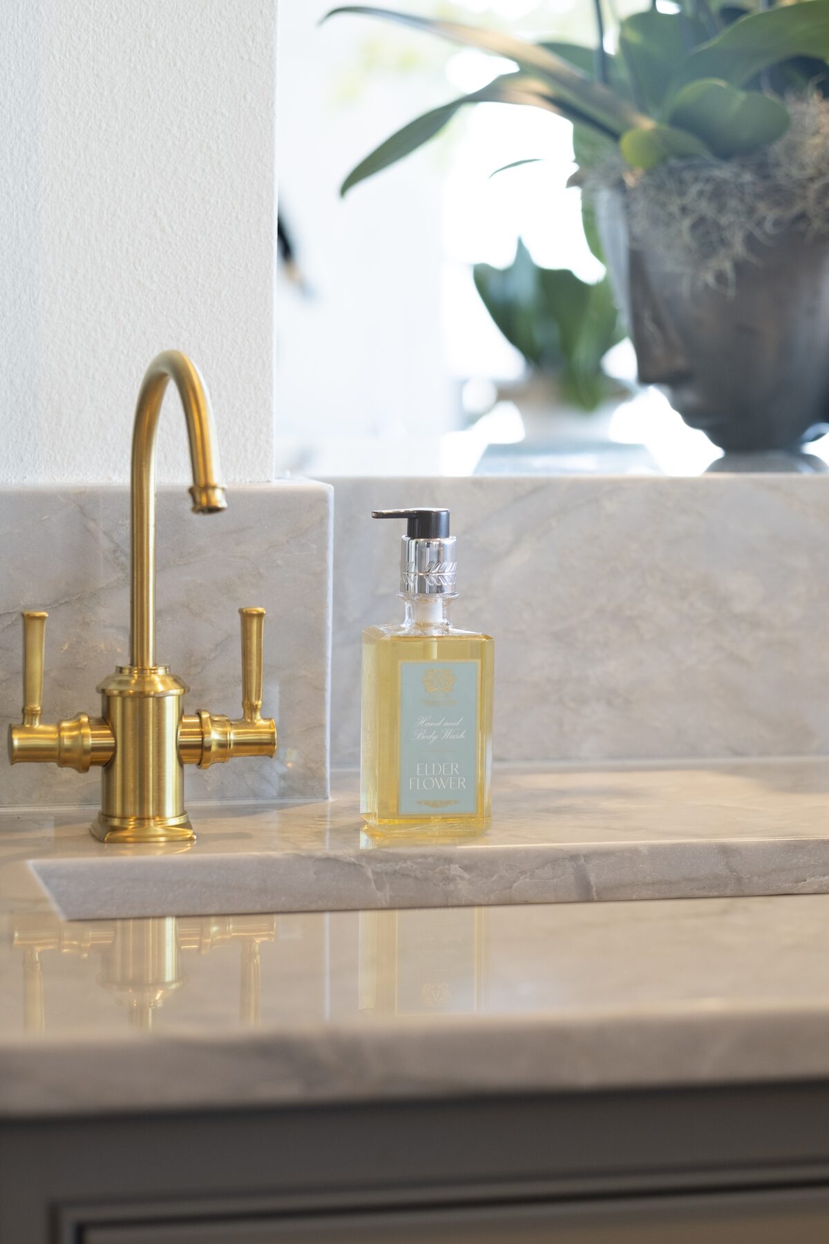 The hand wash at a marble kitchen sink with a brass faucet, orchids behind.