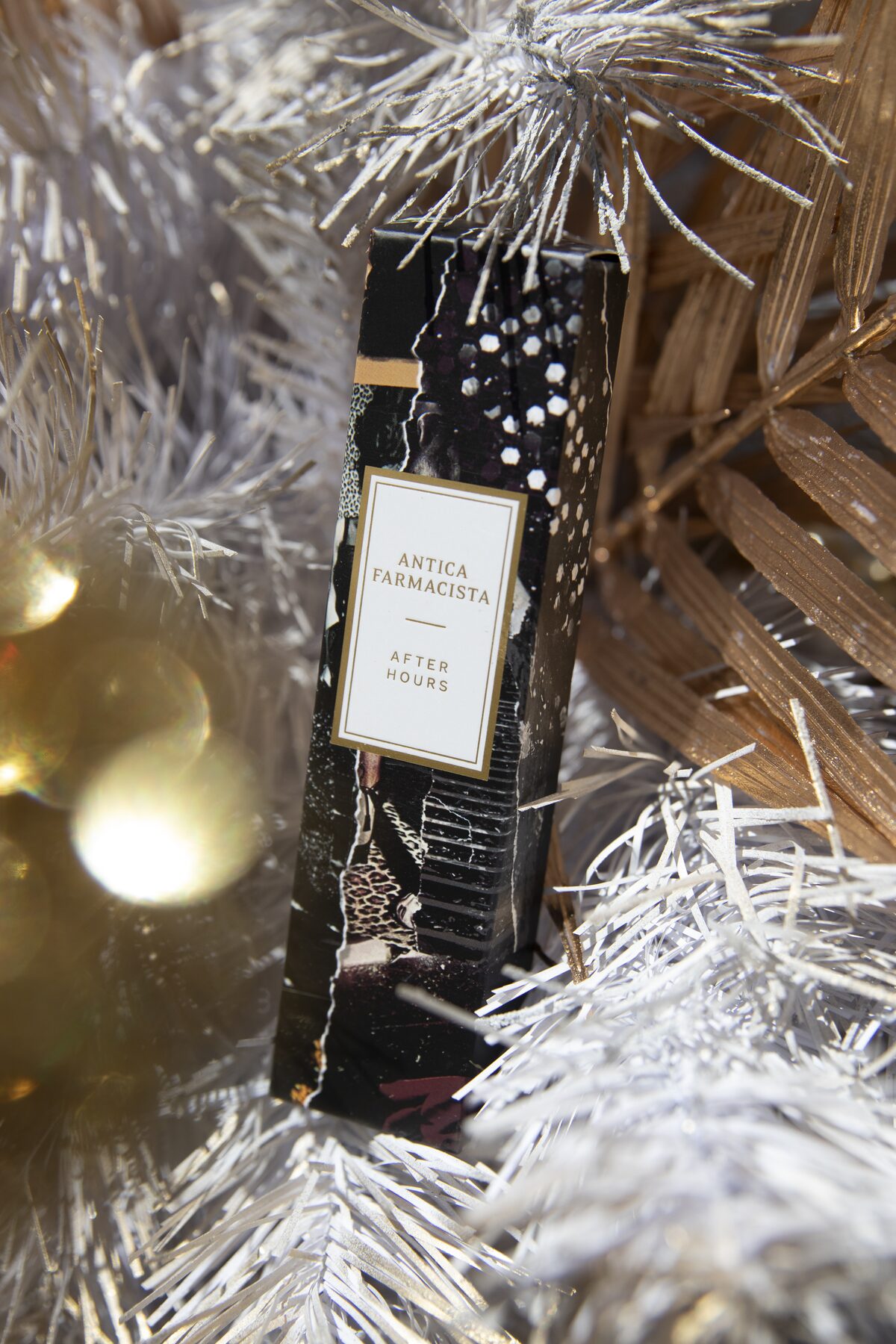The After Hours gift box nestled into the white Christmas tree among gold ornaments and gilded palms.