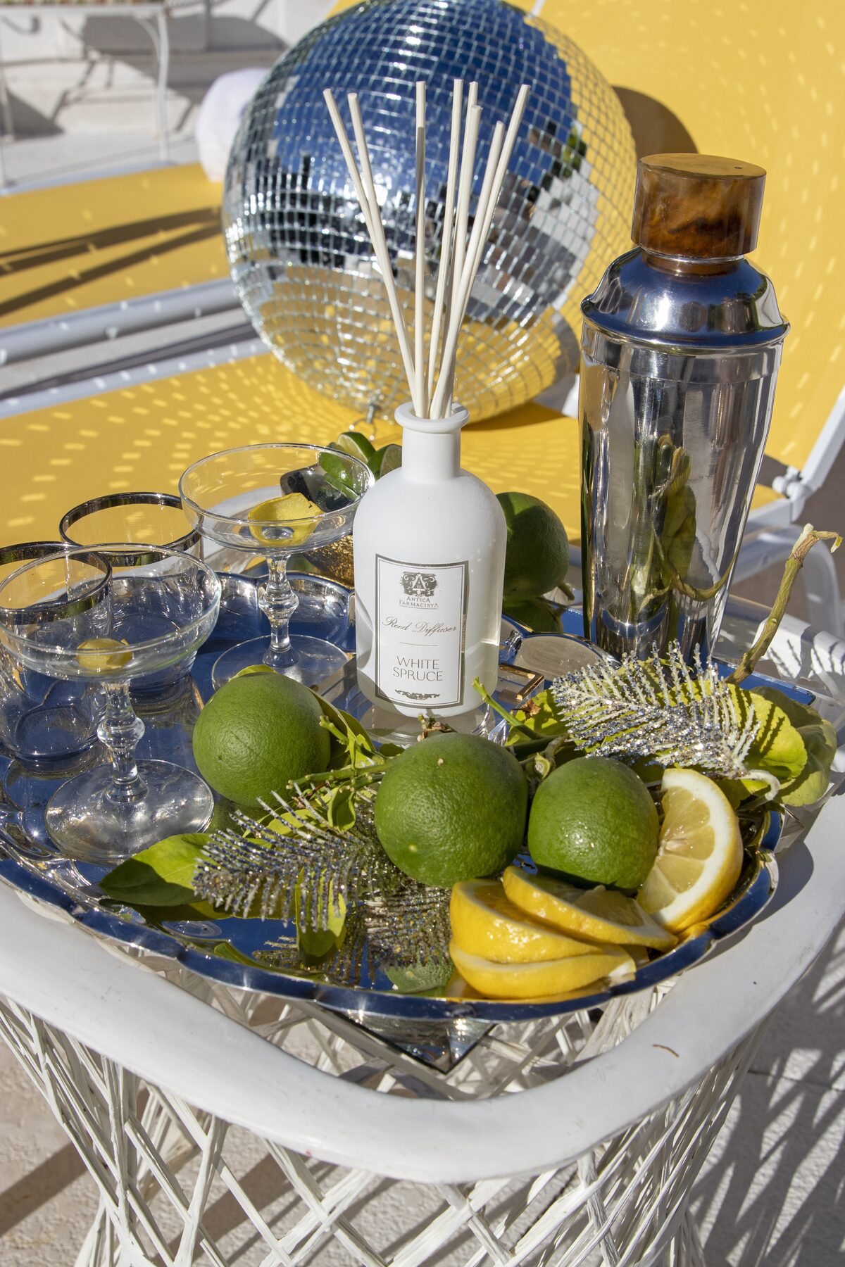 The White Spruce diffuser on a silver tray of limes, lemons, and coupes with a cocktail shaker.