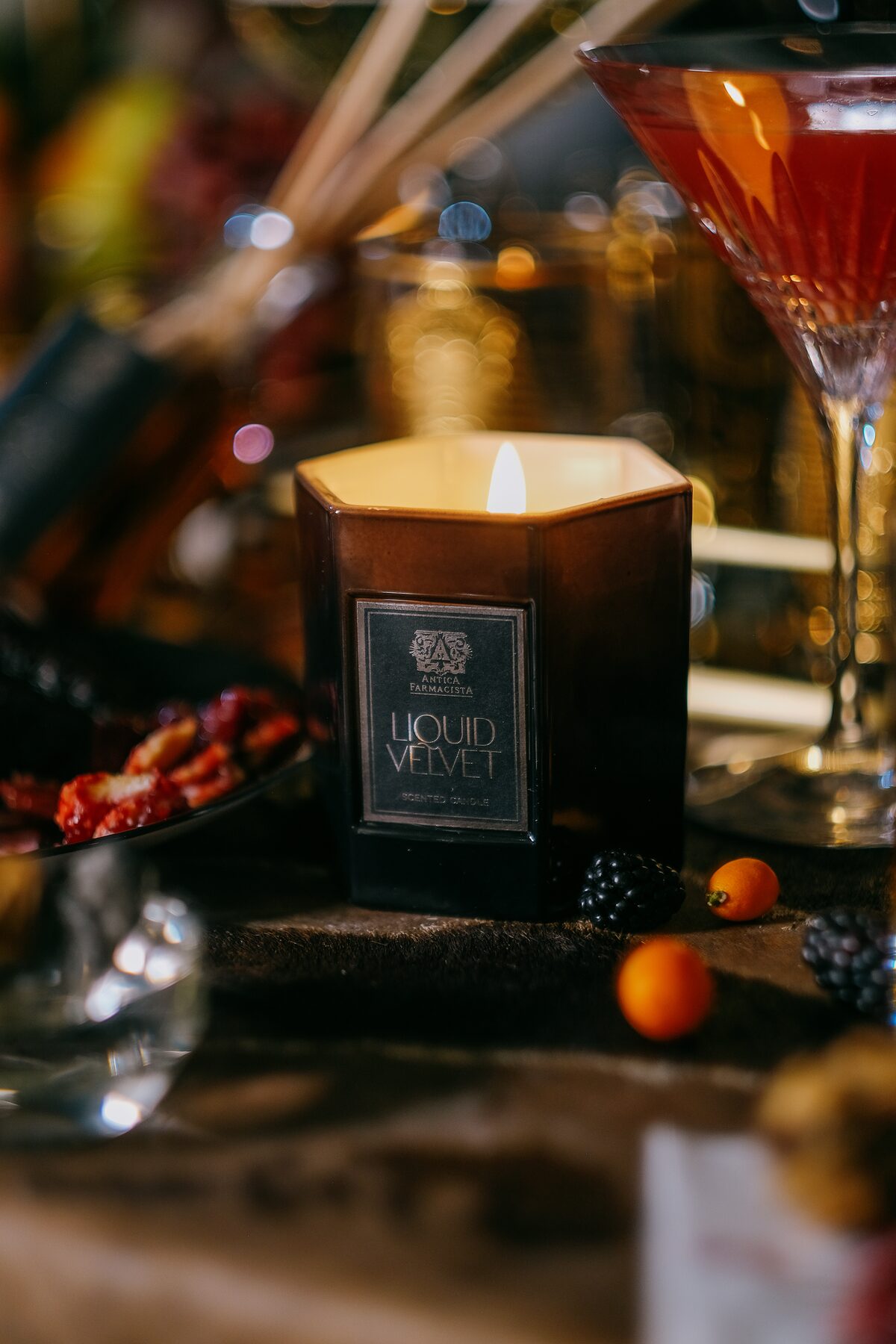 The Liquid Velvet candle in the foreground, a crimson cocktail glowing soft behind.