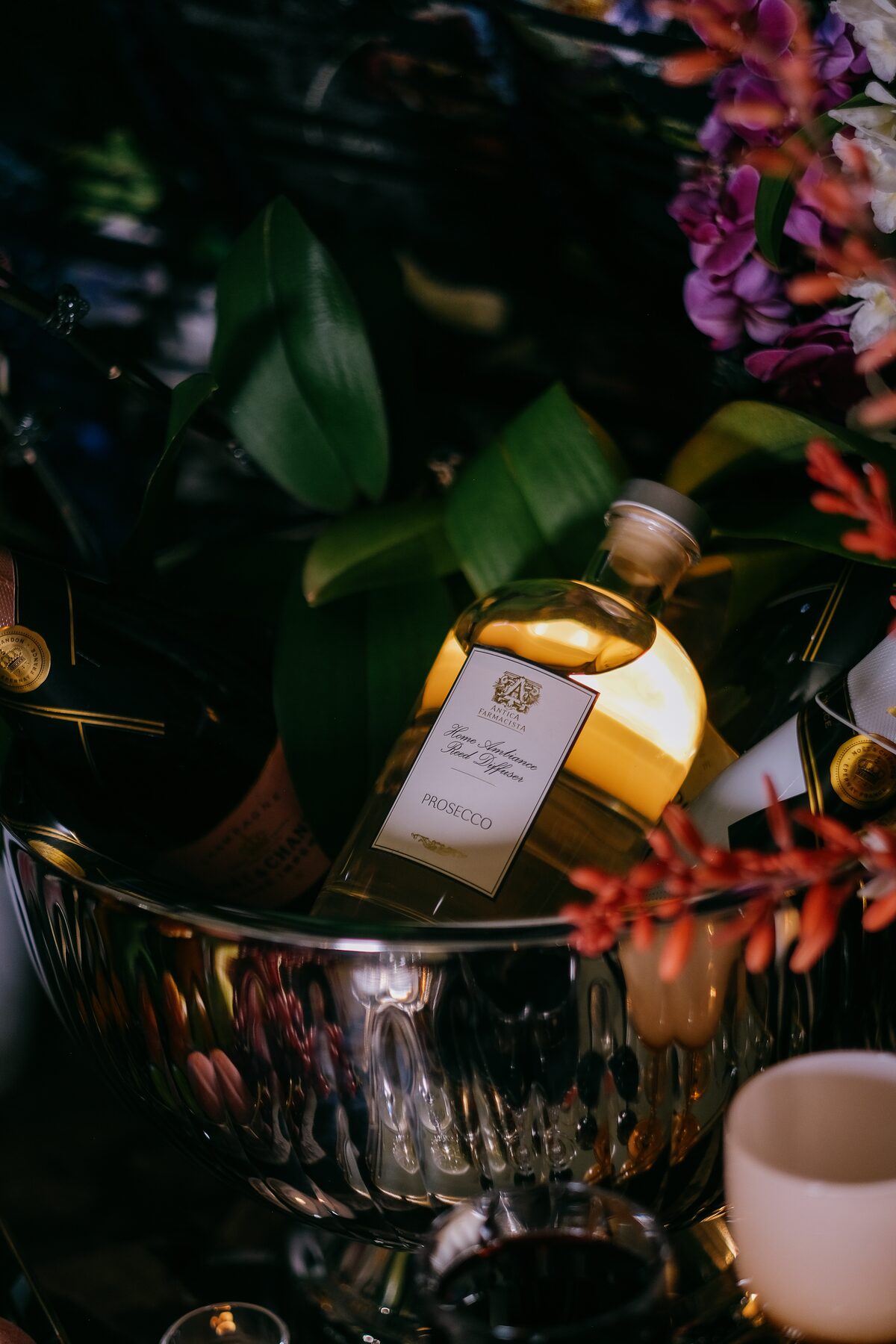 The Prosecco bottle sunk in a silver vessel with greens and a lit candle, deep in shadow.