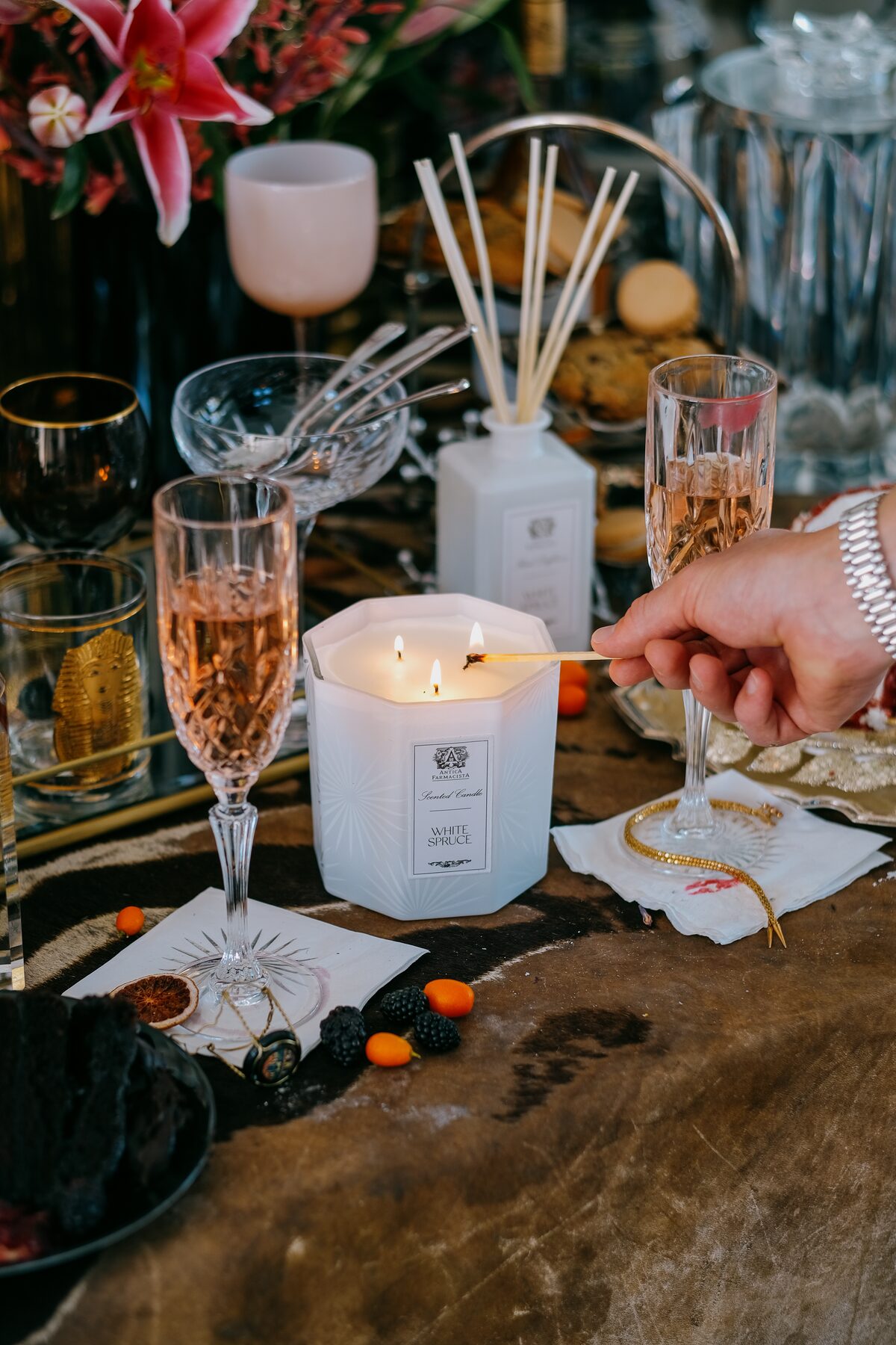 The white three-wick burning at the table’s edge as champagne is poured beyond.