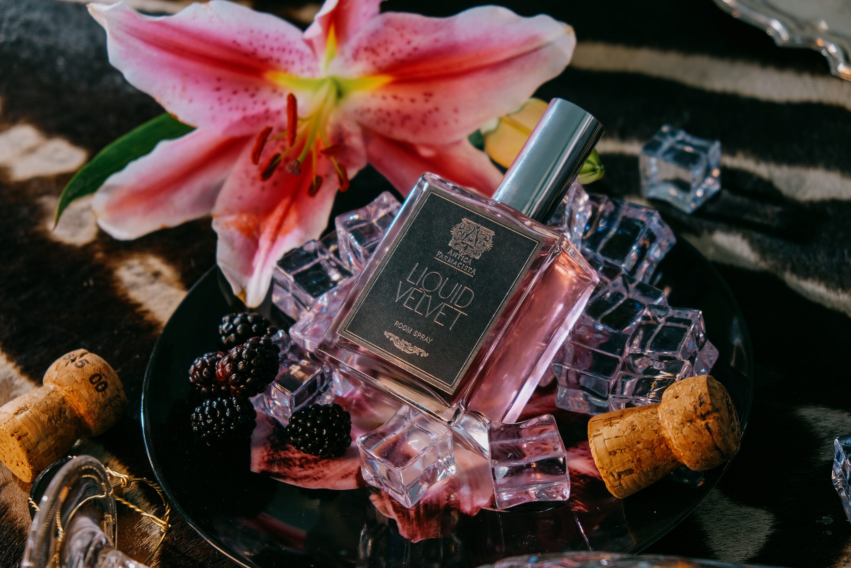 The Liquid Velvet fine fragrance on a crystal tray over zebra hide — stargazer lily, blackberries, ice, and a champagne cork.