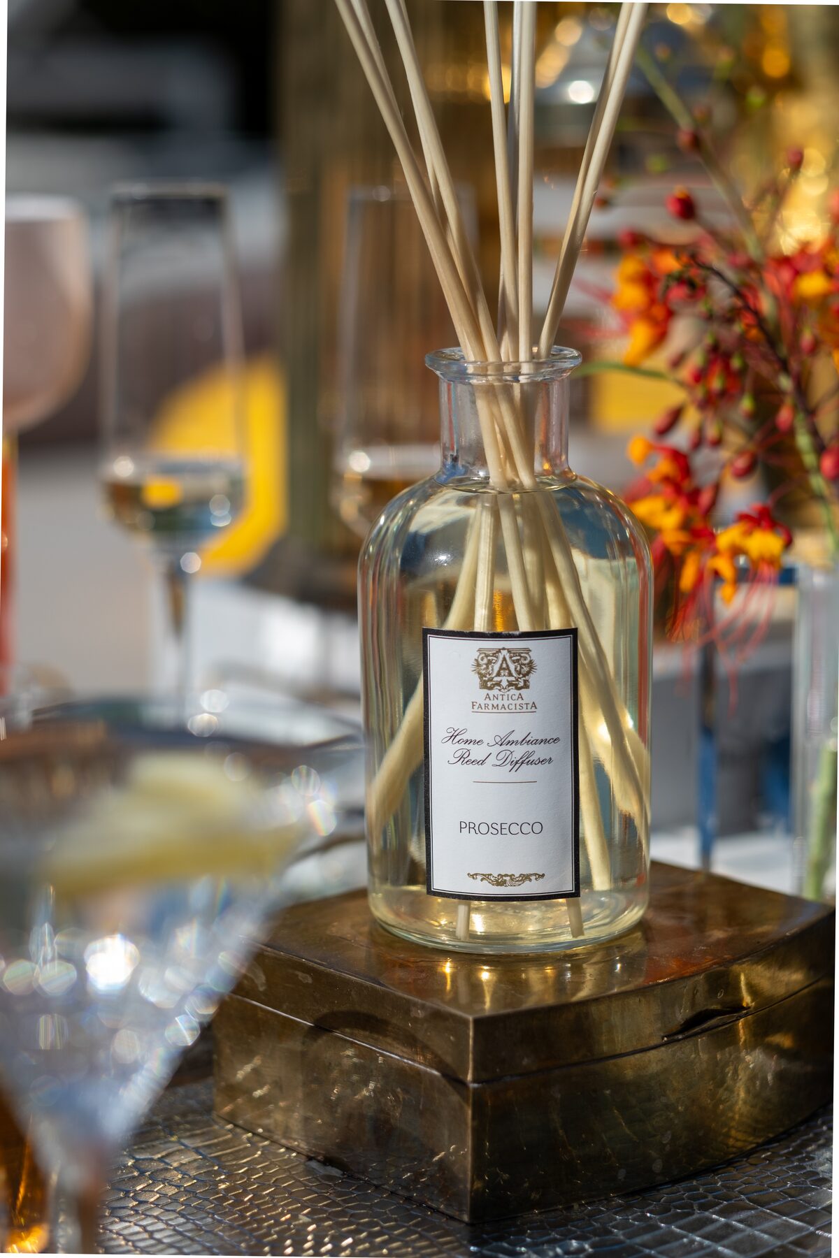 The Prosecco diffuser on its gold box, flame-orange blossom branches behind.