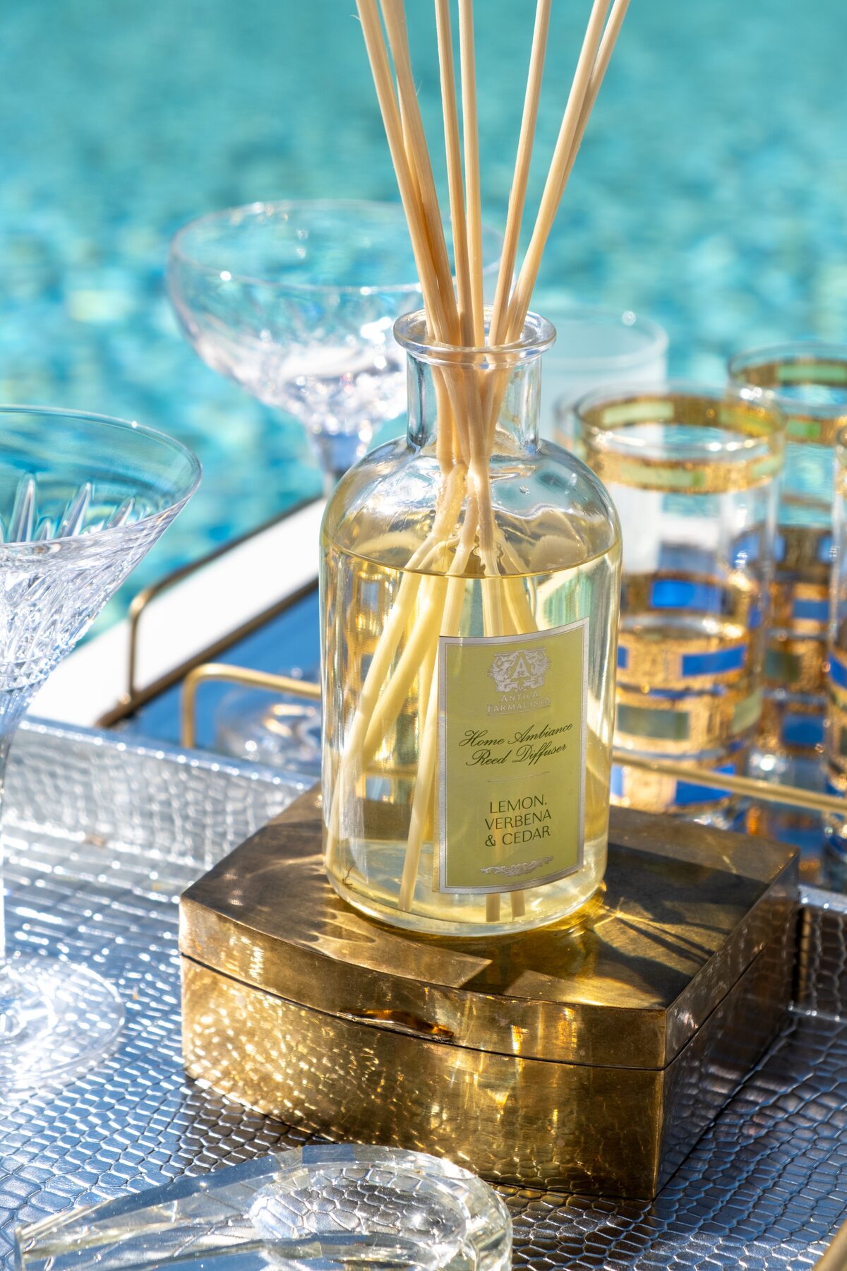 The Lemon Verbena diffuser on its gold box, pool light rippling behind.