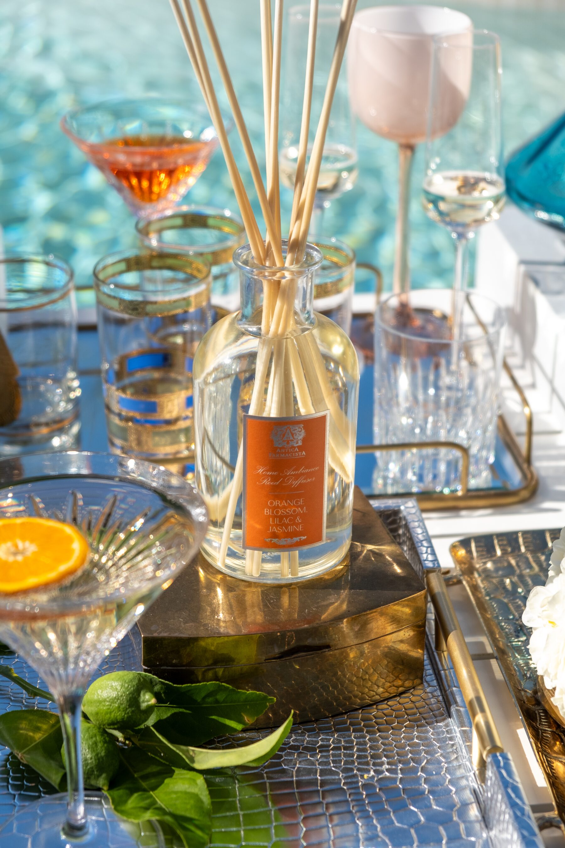 The Orange Blossom diffuser on a gold box at the pool’s edge, coupes and cocktails catching the sun.