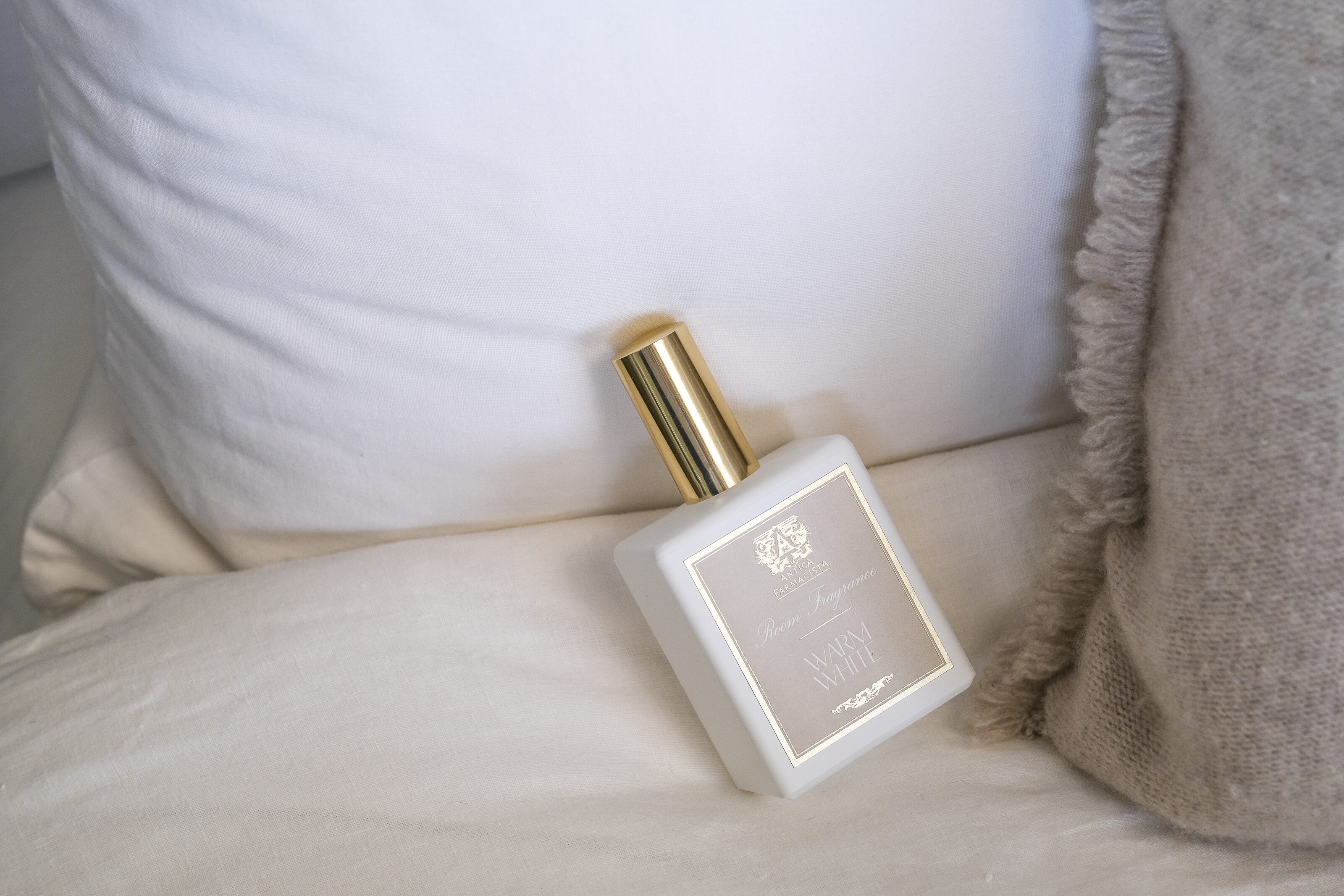 The gold-capped room fragrance at rest against a white pillow, nothing else in frame.