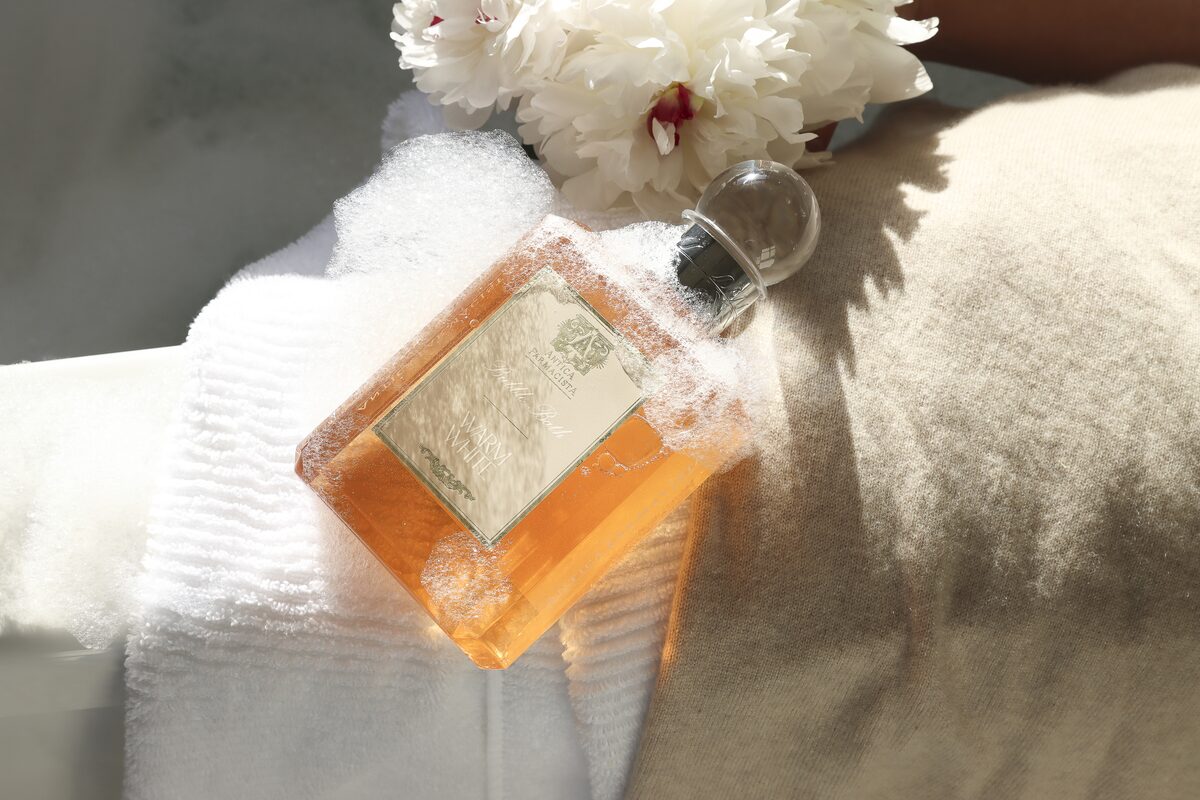 The amber hand and body wash laid into bath foam against soft knit, bubbles clinging to the glass.