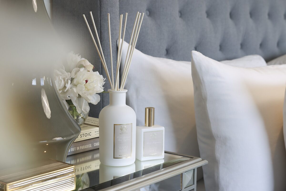 The diffuser and its mini against a grey tufted headboard on a mirrored bedside table.
