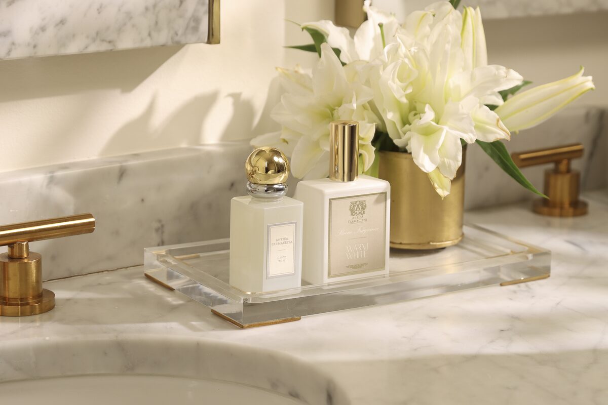 The fine fragrance and wash on an acrylic tray at the marble vanity, lilies in a gold cup by the faucet.