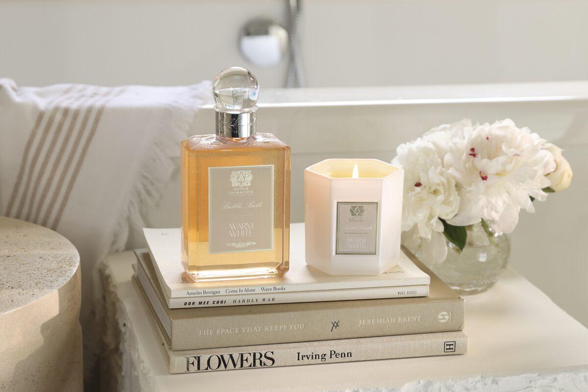 The crystal-stoppered wash and a lit candle stacked on flower books at the bath.