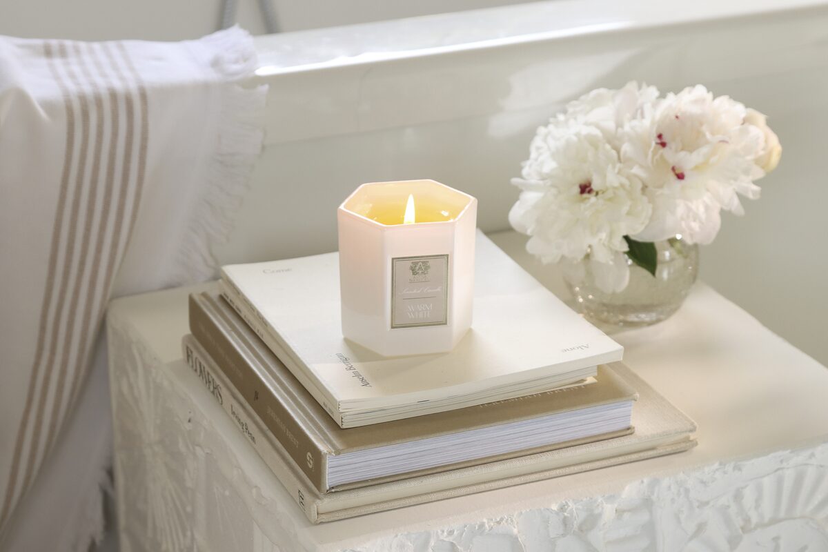 The candle on a stack of art books with a vase of peonies, marble behind.