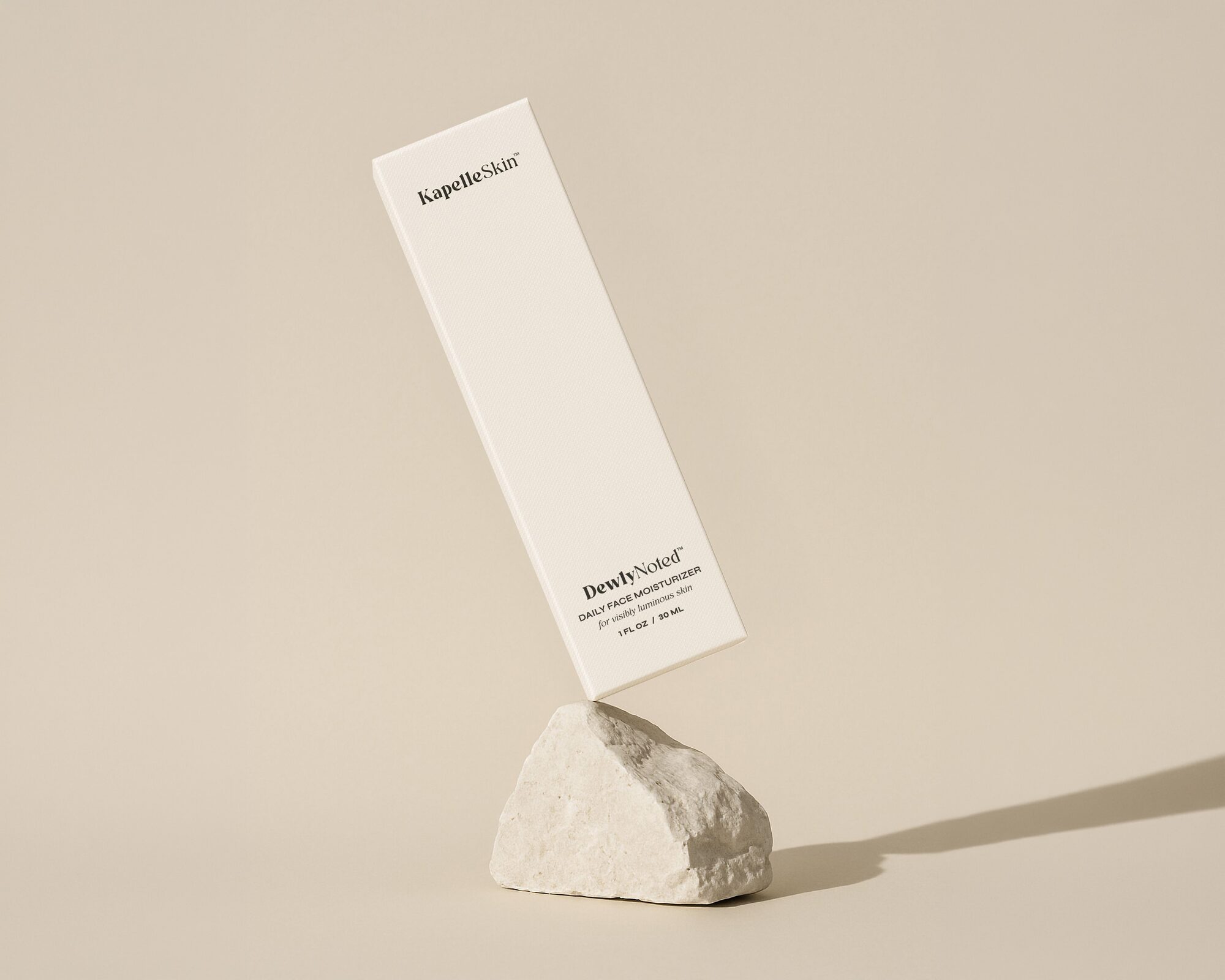 The slim DewlyNoted carton balanced on pale stone against a warm neutral field.