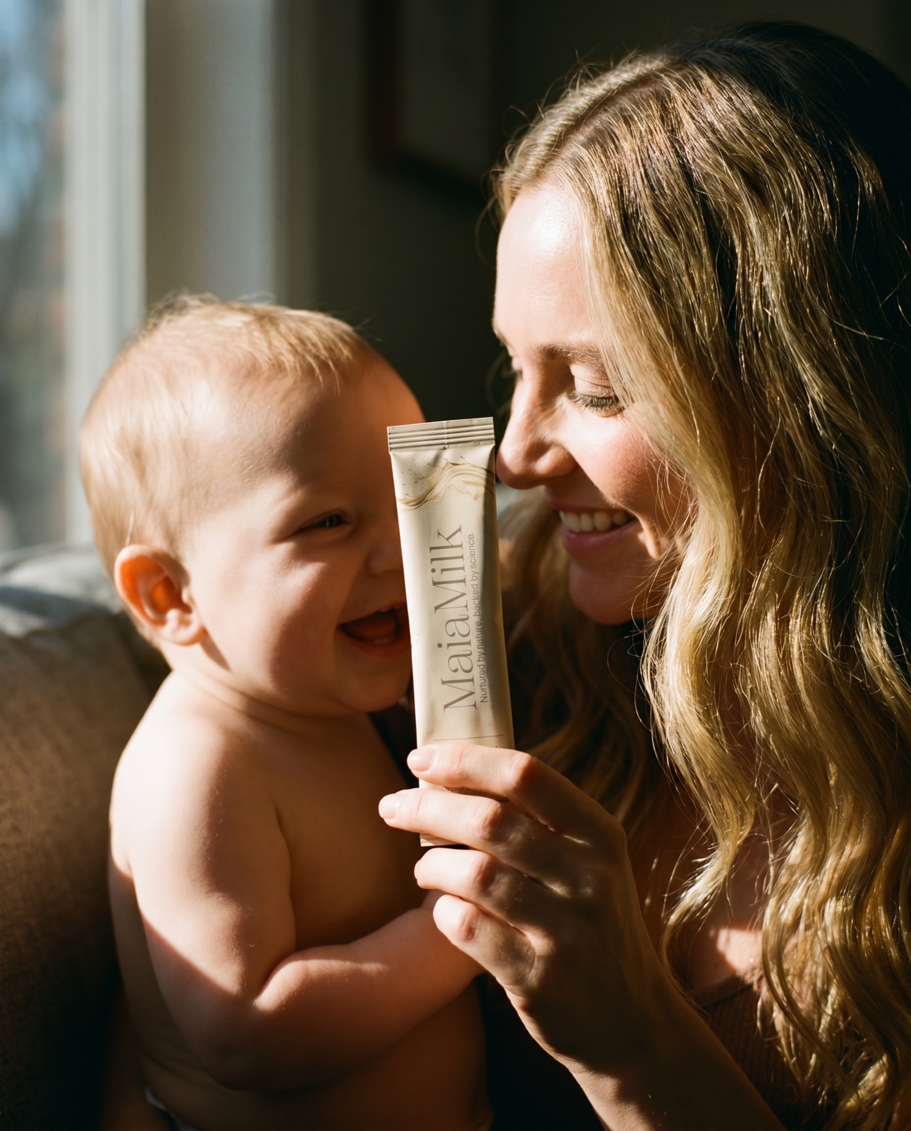 A mother and baby smile together with a MaiaMilk packet held between them.
