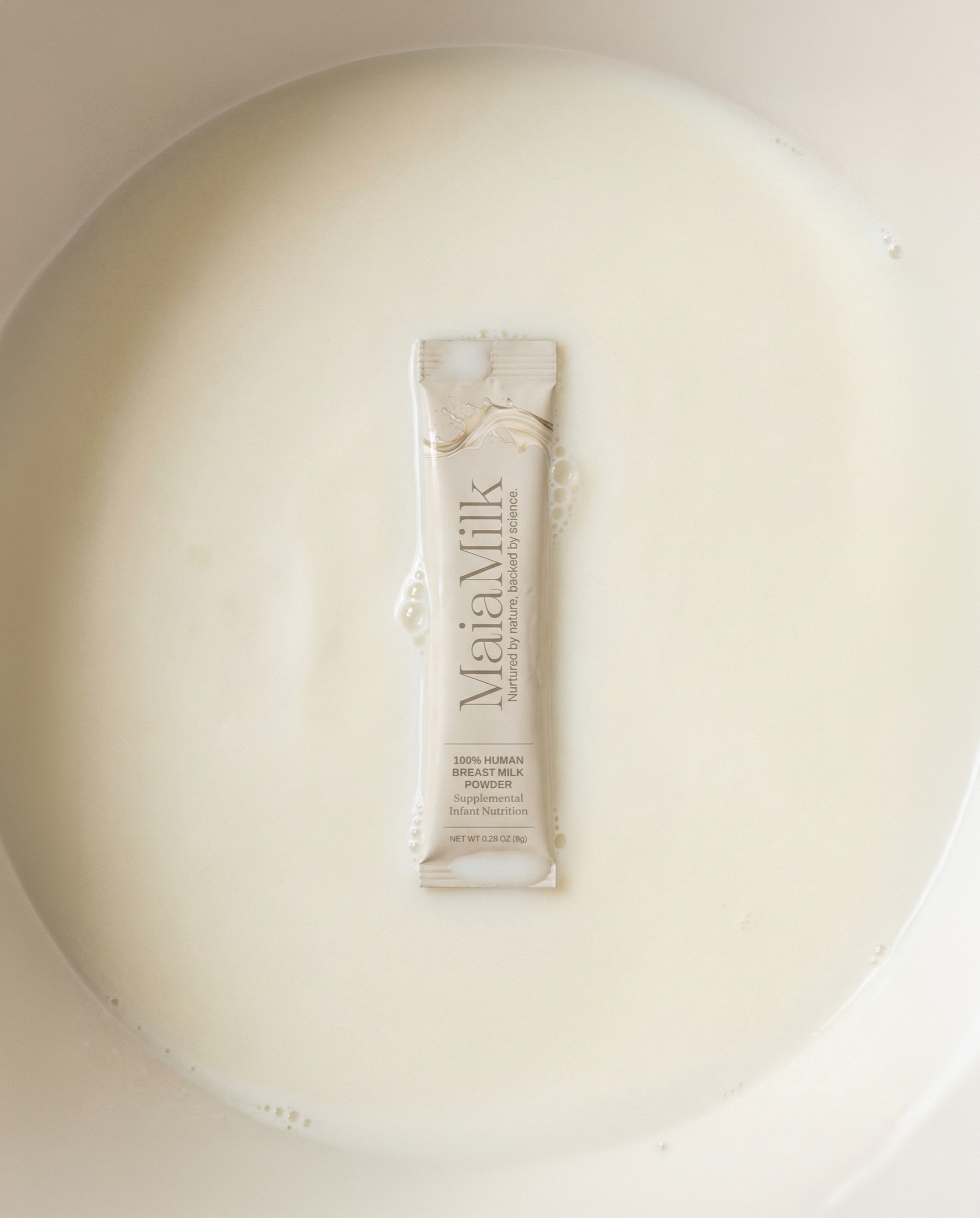 A MaiaMilk packet lies in a shallow pool of milk with a wide cream field around it.